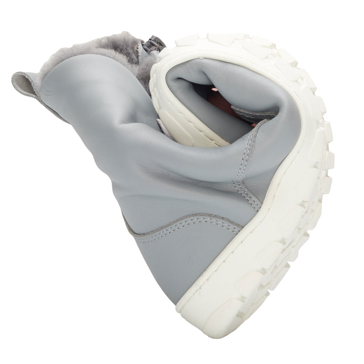 De QUINTIC Winter Blue Grey van ZAQQ is een flexibele winterlaars in grijs met een dikke witte zool, die in het midden gebogen is om de buigzaamheid te benadrukken. De laars is gemaakt van zacht nappaleer en binnenin uitgerust met een knusse, pluizige voering.