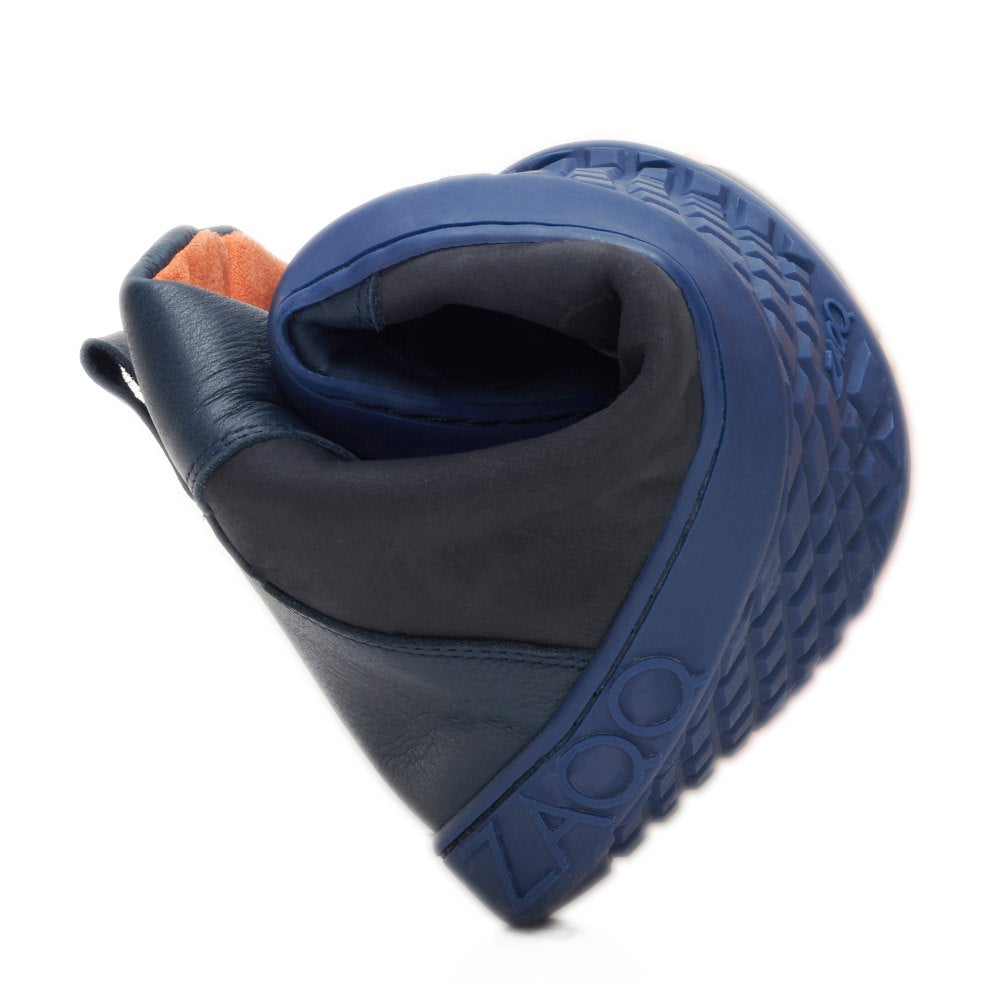 De WALQER Navy van ZAQQ is een flexibele schoen in blauw met een gestructureerde zool die zijn buigzaamheid bij het buigen benadrukt. Deze barefoot boot van hoogwaardig nappaleder heeft contrasterende zwarte en oranje elementen die zijn unieke en stijlvolle design accentueren.