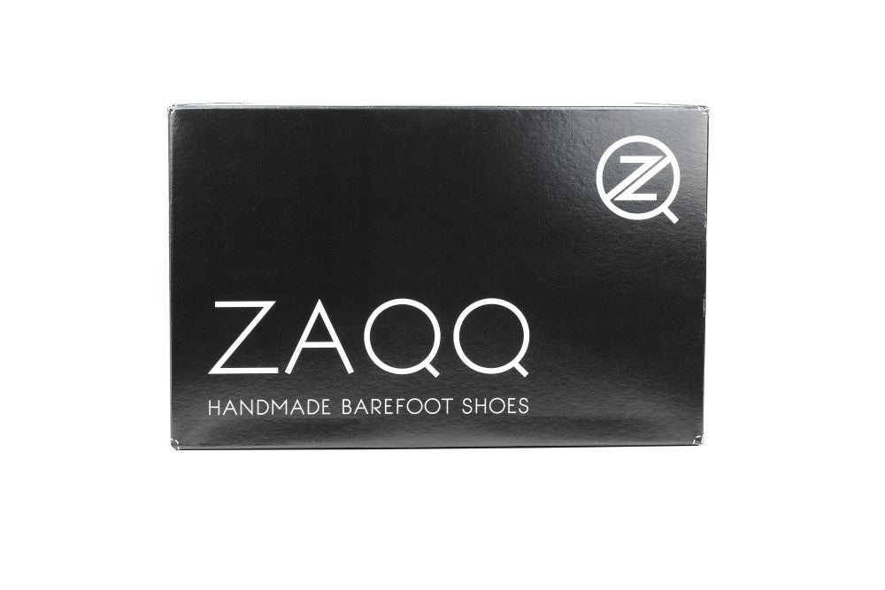 Op een zwarte, rechthoekige schoenendoos is de grote witte tekst 'ZAQQ' duidelijk te zien. Daaronder zijn de woorden 'Handmade Barefoot Shoes' te zien, wat hem perfect maakt voor outdoorliefhebbers die op zoek zijn naar barefoot outdoorlaarzen. In de rechterbovenhoek wijst een cirkelvormig logo met een gestileerde Z subtiel op het duurzame ontwerp van de trailzool van ROQQ Trail Black.