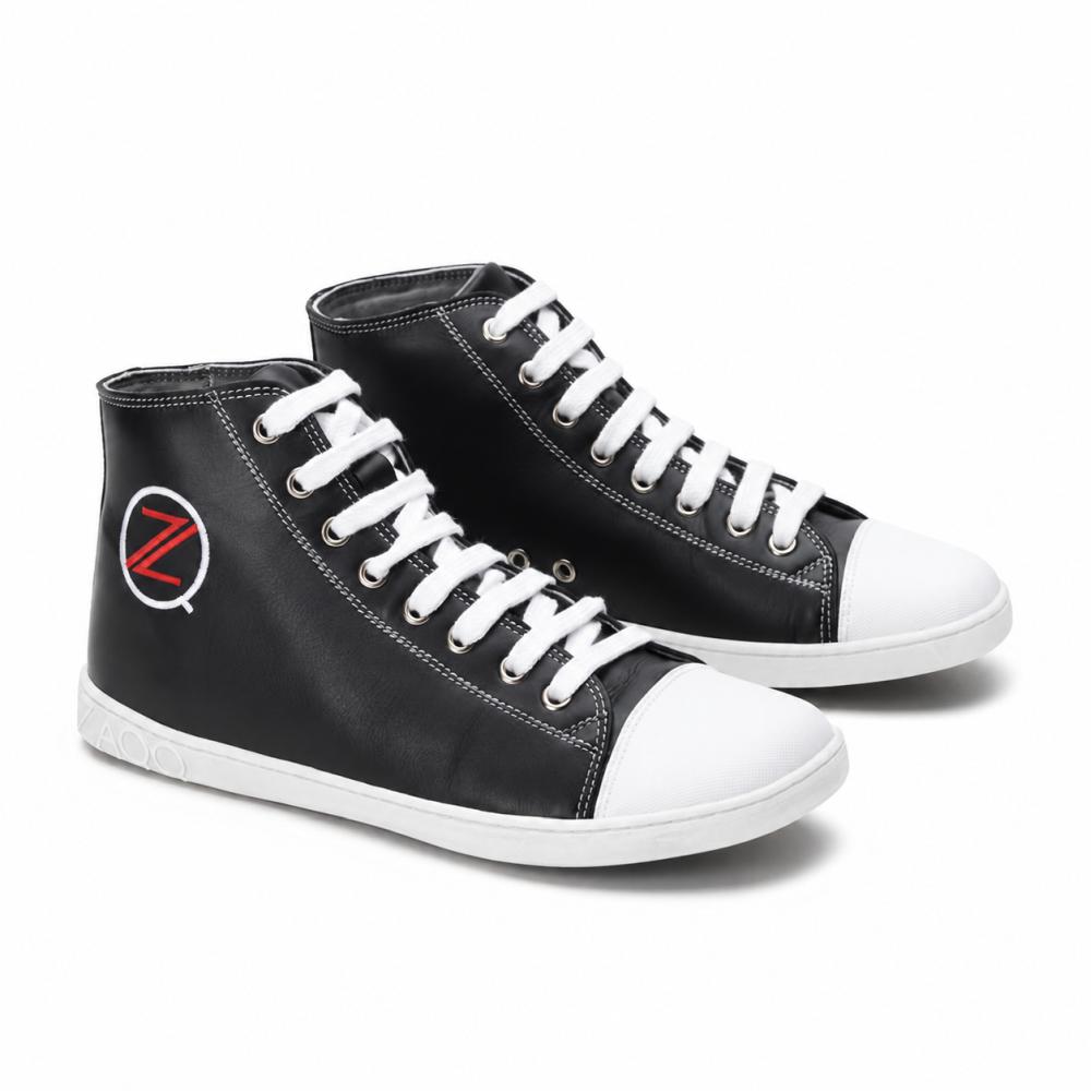 Een paar klassieke zwarte high-top sneakers van ZAQQ CHUQQS heeft witte veters en neuskappen, die elk een opvallend rood-wit Z-logo tonen. De zolen zijn gemaakt van duurzaam rubberen zool, wat de schoenen een trendy, licht versleten look geeft.