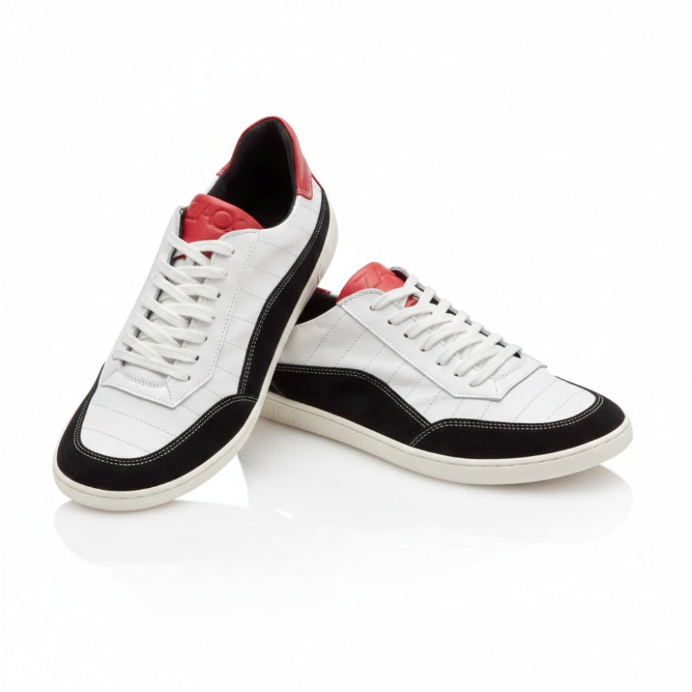 Wir präsentieren den eleganten QAMPION Black White von ZAQQ. Dieser stylische Barfuß-Sneaker zeichnet sich durch dynamische weiße, schwarze und rote Details aus und hat flexible Sohlen für mehr Komfort. Er verfügt über strahlend weiße Schnürsenkel, glatte schwarze Seiten und auffällige rote Akzente an Zunge und Ferse. Ein Schuh wird aufrecht präsentiert, während sein Partner anmutig dagegen lehnt.