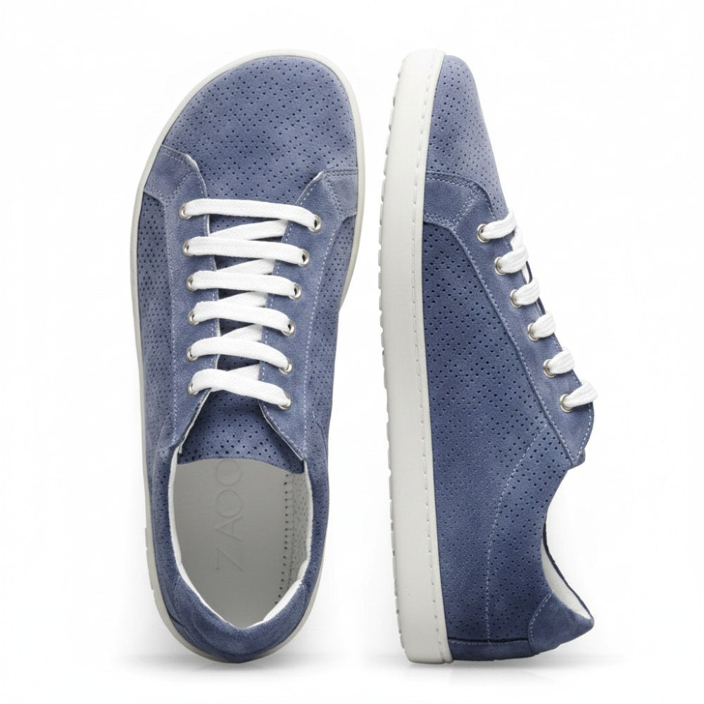 Ein Paar SLOQ Blue Sneaker von ZAQQ aus blauem Veloursleder mit auffälligen weißen Schnürsenkeln und Sohlen, mit perforiertem Design und dem Logo der Marke an der Seite. Ein Sneaker steht aufrecht, während der andere auf der Seite liegt.