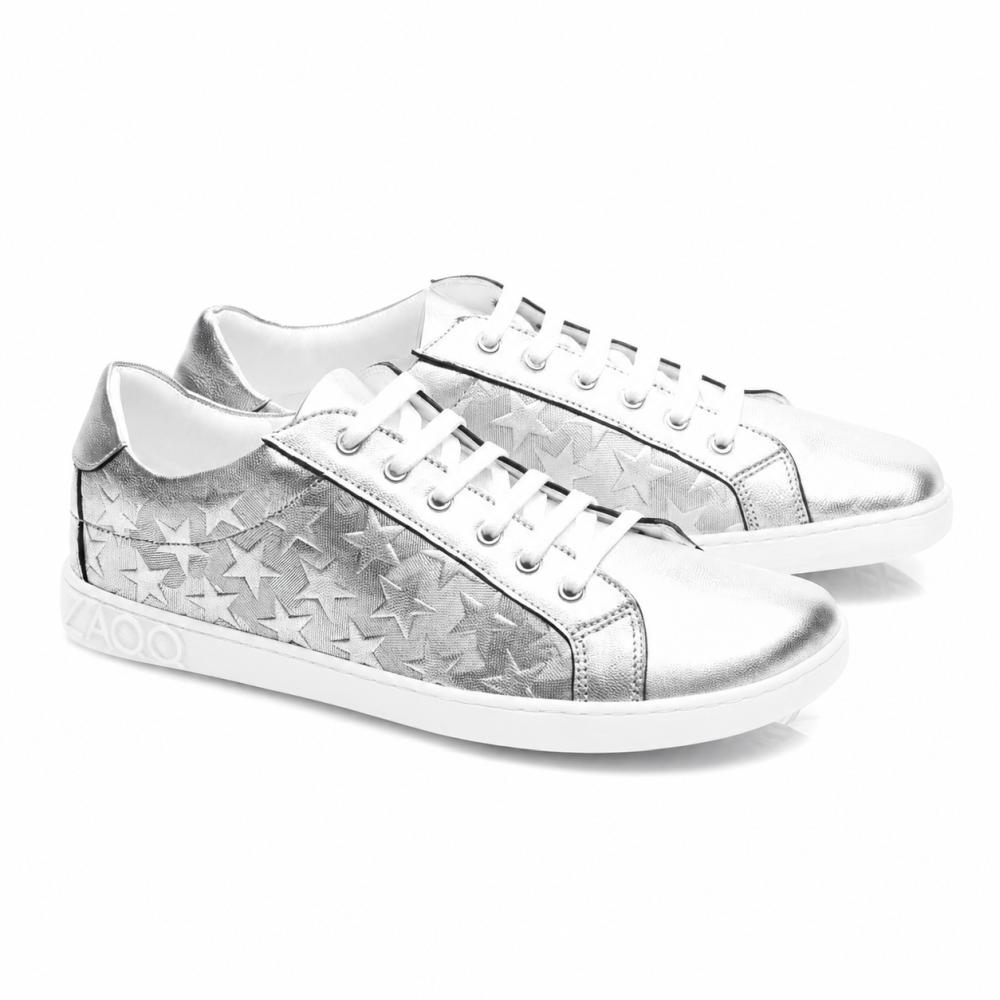 De SLOQ Stars Silver-Sneaker van ZAQQ hebben witte veters en sterpatronen aan de zijkanten, aangevuld met een witte zool met VAOO-embossing op de hiel. Deze schoenen kenmerken zich door een slank en modern design met een glanzende metallic afwerking.