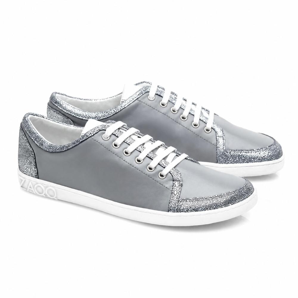 De TIQQ Grey Silver Sneaker van ZAQQ vallen op door hun eenvoudige ontwerp van zacht nappaleer met witte veters en zilveren glitteraccenten, aangevuld met witte zolen en een subtiel logo op de hiel, en bieden de perfecte mix van stijl en comfort voor elke gelegenheid.